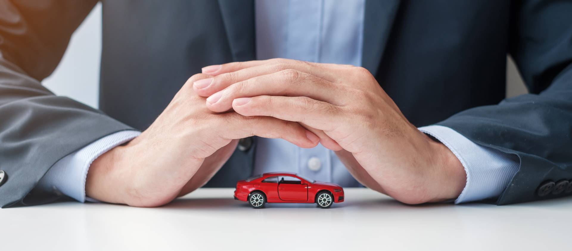 Businessman hands covering over a toy car.