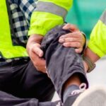 Construction worker receiving assistance after suffering a leg injury at a construction site.