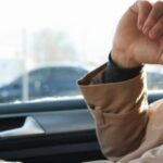Driver appearing fatigued while operating a vehicle, resting a hand near their face during a daytime drive.