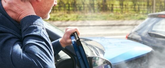 Man experiencing neck pain after a car accident while standing beside a damaged vehicle