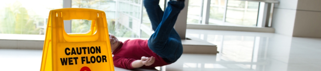 Person slipping on a wet floor next to a caution sign, illustrating a slip and fall accident that may result in a personal injury claim.