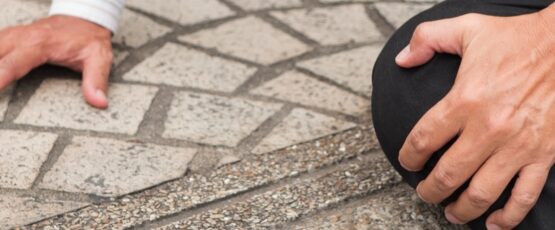 Person holding their knee after tripping on an uneven sidewalk, illustrating a premises liability accident caused by unsafe property conditions.