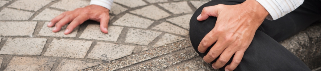 Person holding their knee after tripping on an uneven sidewalk, illustrating a premises liability accident caused by unsafe property conditions.