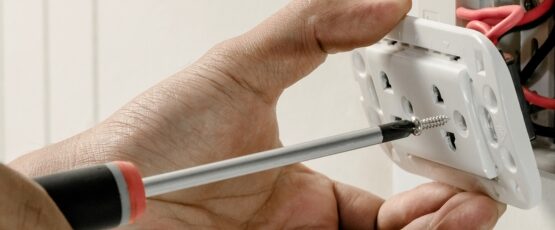 Person using a screwdriver to install an electrical outlet while working on home electrical wiring