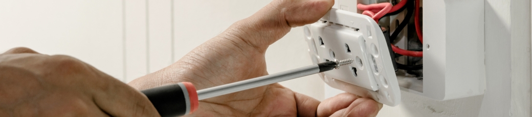 Person using a screwdriver to install an electrical outlet while working on home electrical wiring