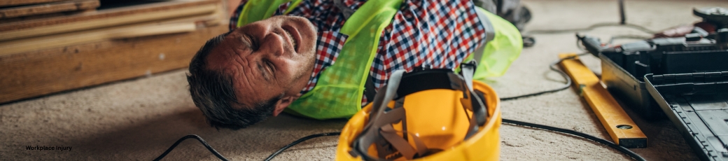 Construction worker lying injured on a worksite beside a hard hat and power tools after a workplace accident.